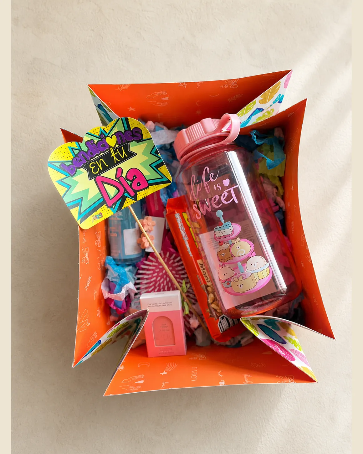 Caja de regalo abierta en naranja con cartel bendiciones en tu día, botella térmica, snacks y detalles de cuidado personal