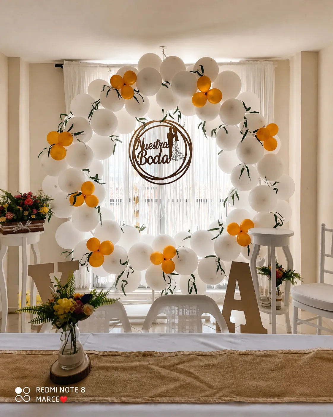 Aro de globos blancos y dorados con cartel de nuestra boda y flores