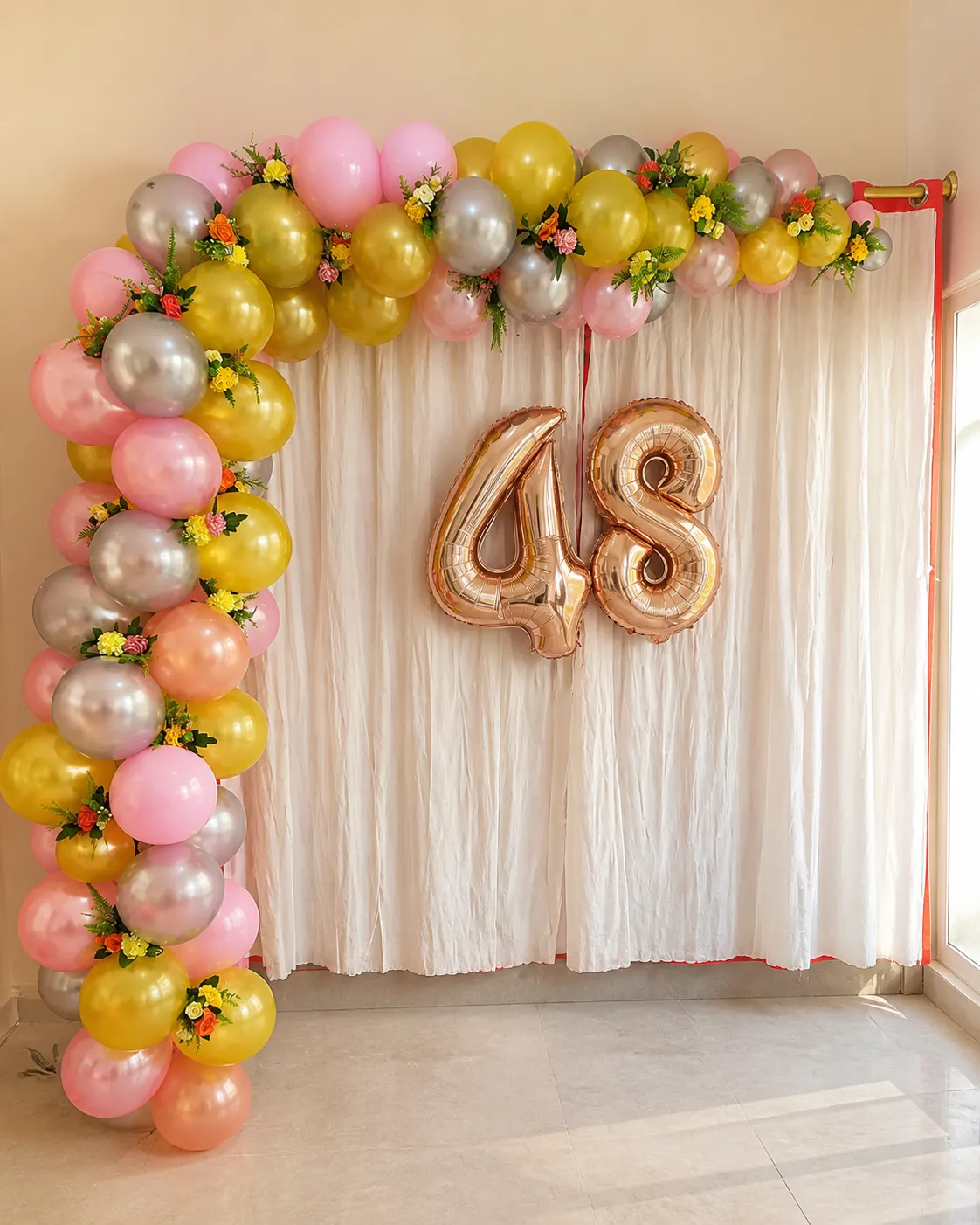 Arco orgánico de globos en melocotón, amarillo y rosa con número metalizado sobre cortina nude